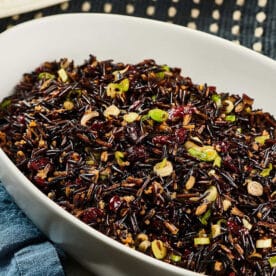White serving dish filled with wild rice and cranberry salad on table.