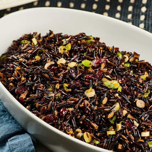 White serving dish filled with wild rice and cranberry salad on table.