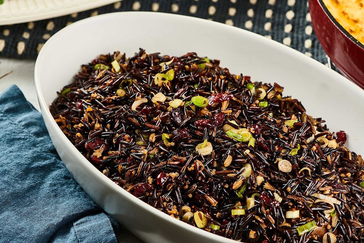 White serving dish filled with wild rice and cranberry salad on table.