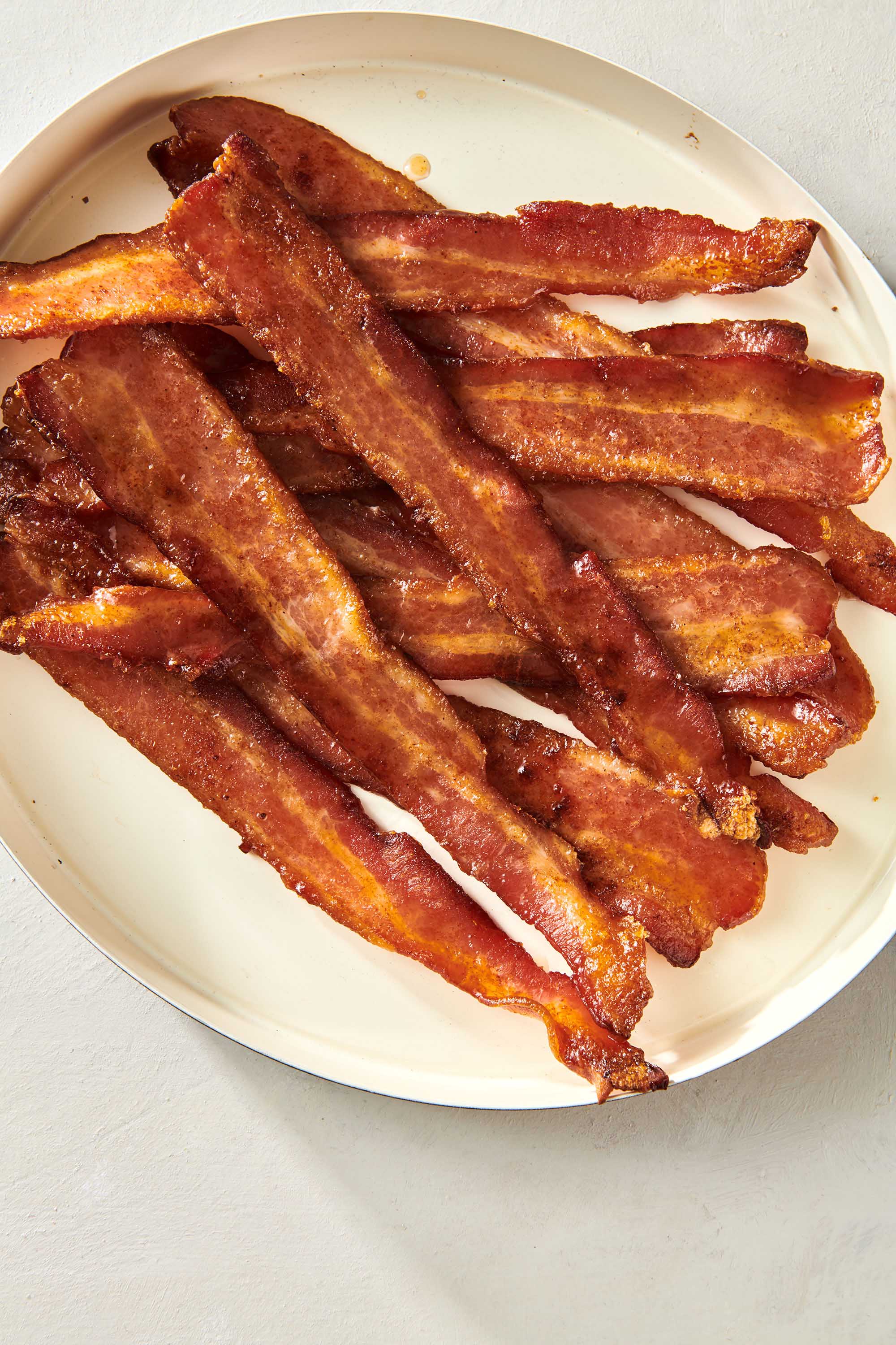 Slices of Candied Bacon piled on a plate.