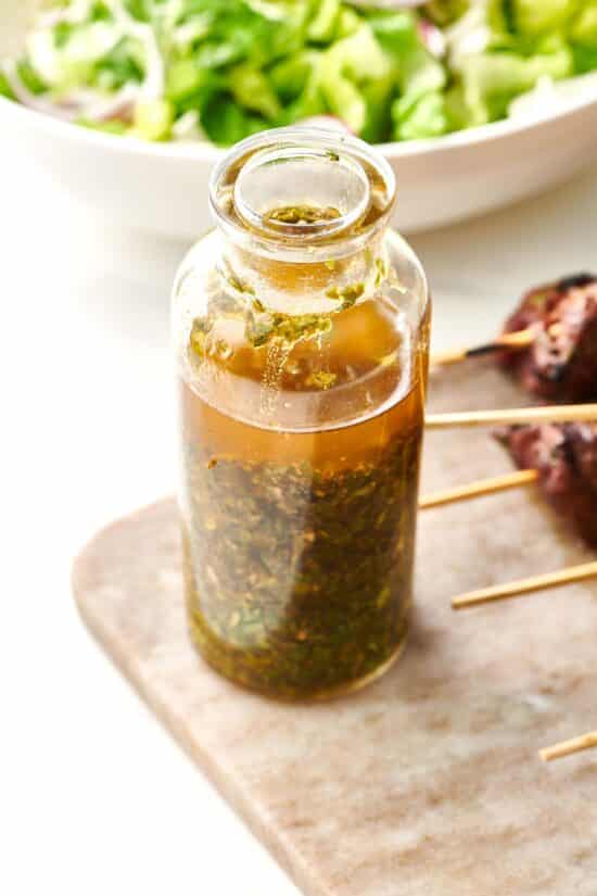 Glass jar of Chermoula next to skewered meat.
