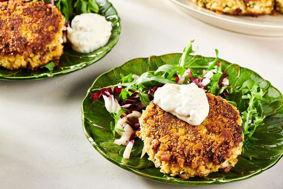 Green plate with a Crab Cake topped with tartar sauce.