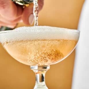 Champagne pouring into a long-stemmed glass for a French 75.