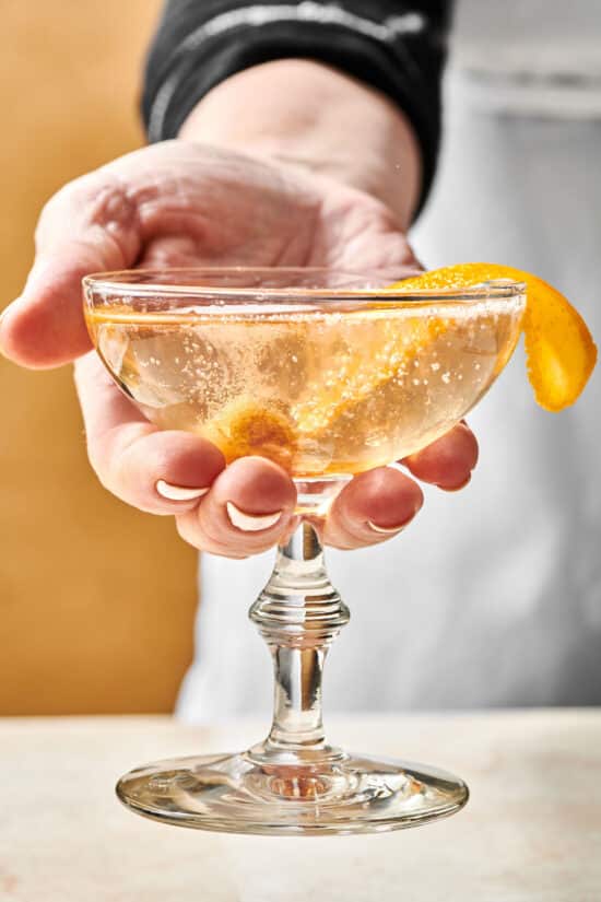 Woman holding a French 75 in a long-stemmed glass with an orange peel.