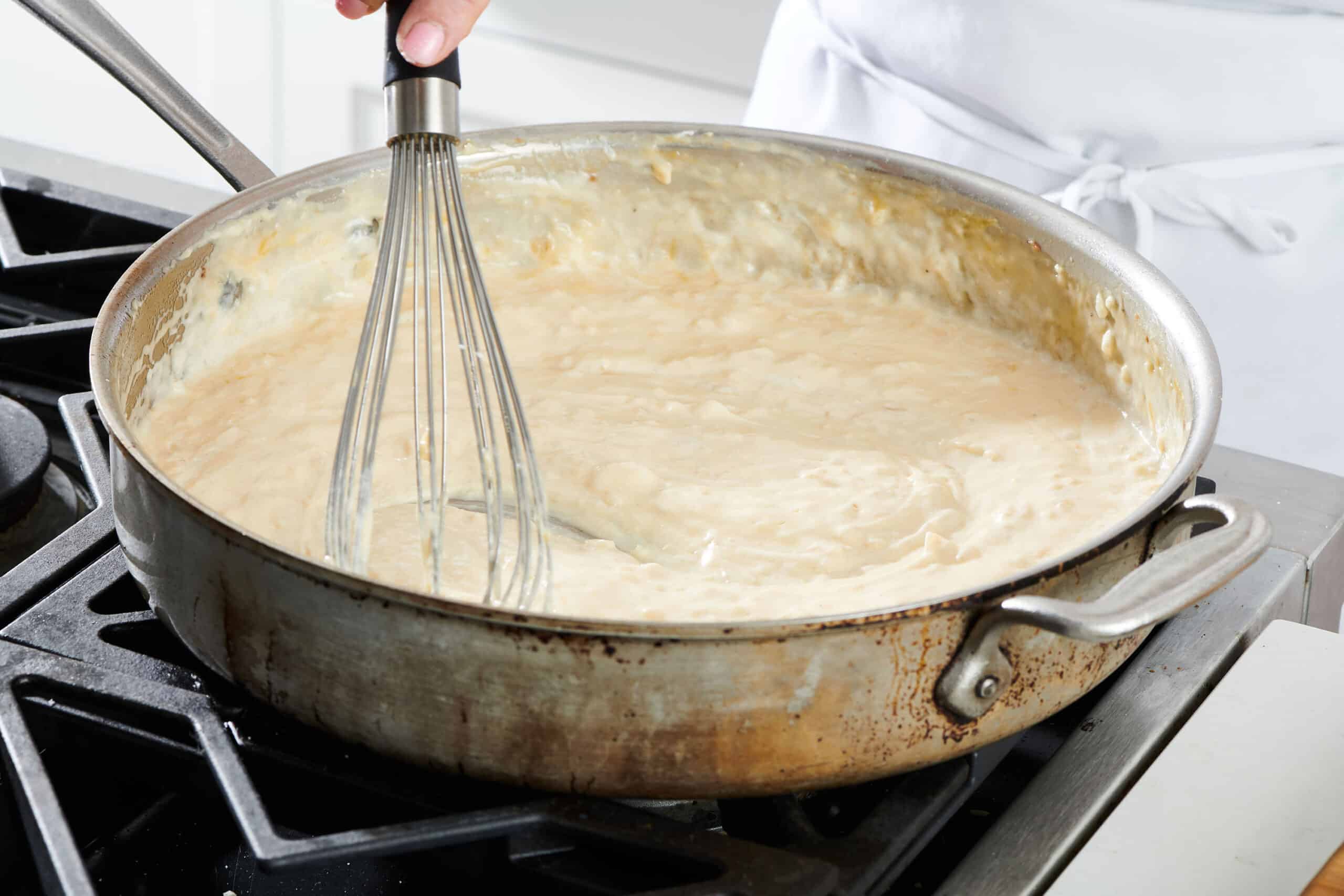 Flour and milk mixture being whisked in a skillet.