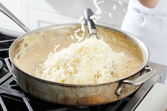 Shredded cheese being added to a skillet.