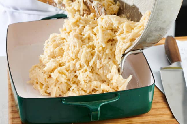 Wooden spoon scooping funeral potato mixture into a baking pan.