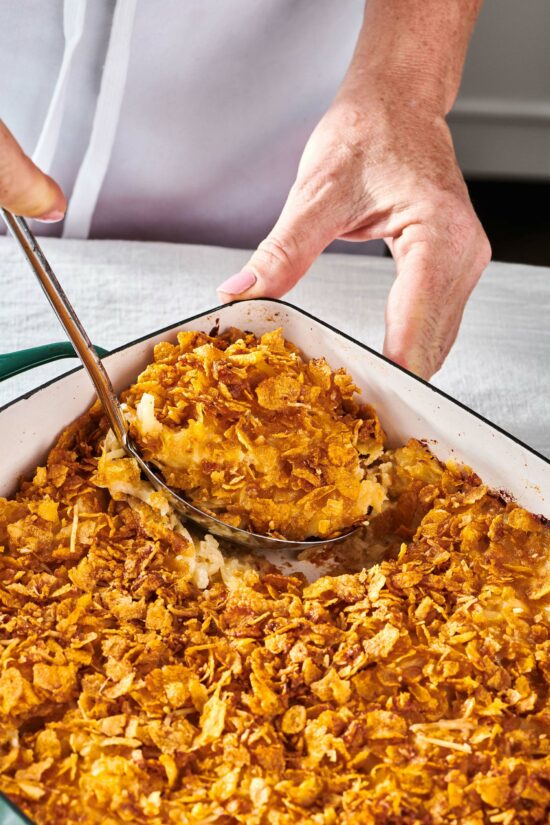 Woman using a ladle to scoop Funeral Potatoes.