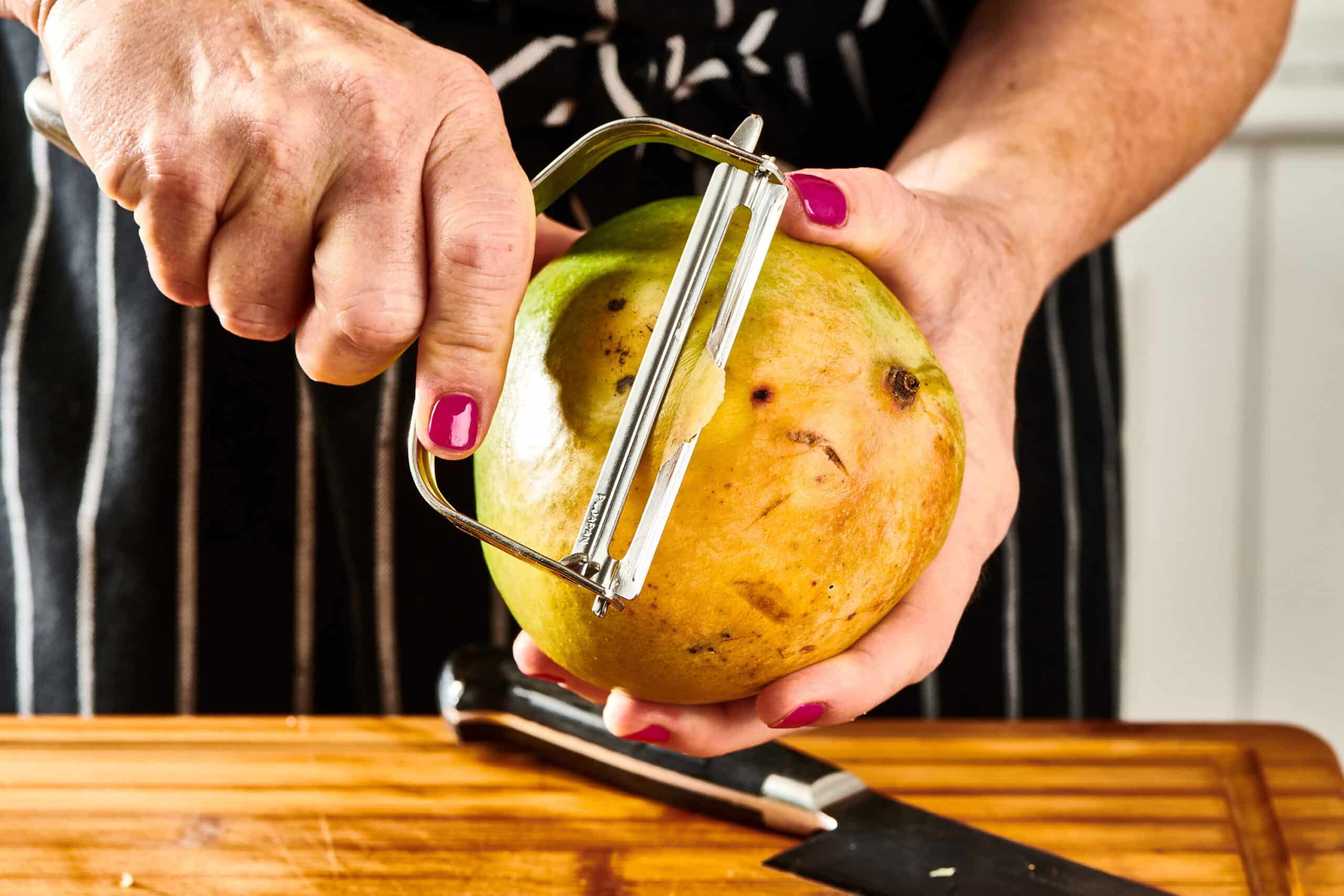 Woman using a peeler to peel a mango.