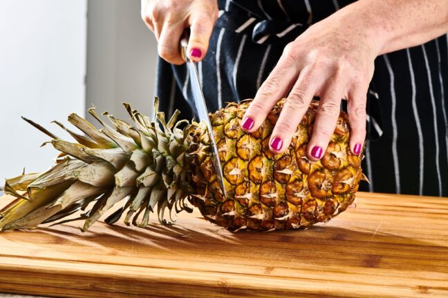 Woman cutting the top off of a pineapple.