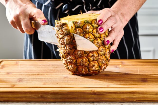 Woman slicing the outside off of a pineapple.