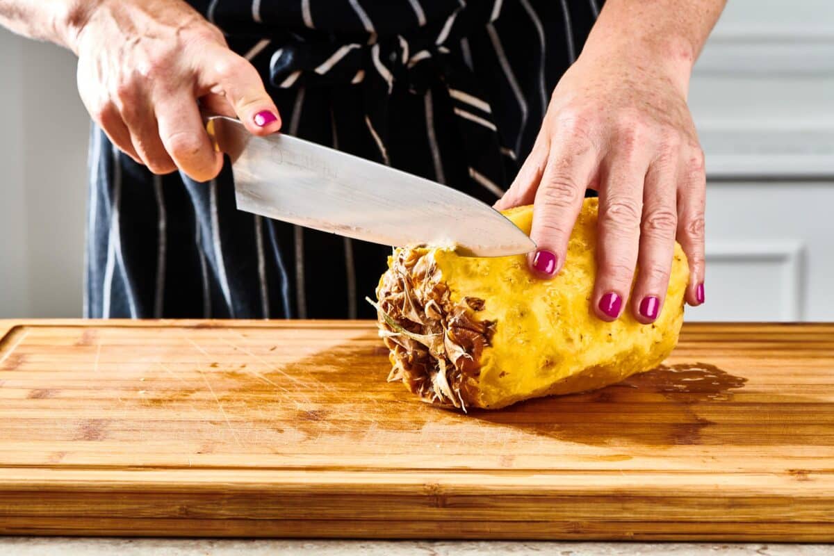 Woman cutting pineapple with chef knife.