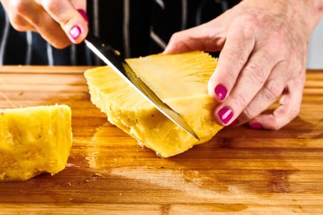 Woman using a knife to take the core out of a pineapple.