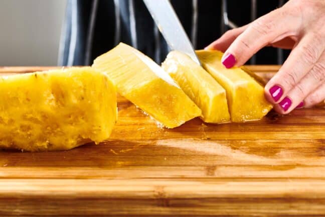 Woman cutting a peeled pineapple into long slices.