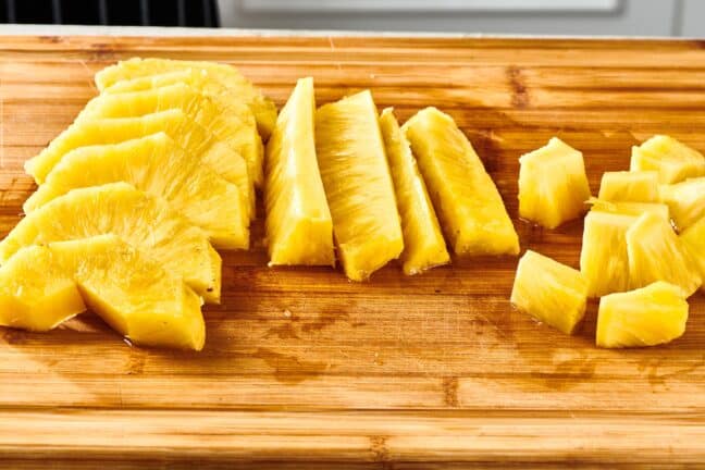 Various sized pieces of pineapple on a cutting board.