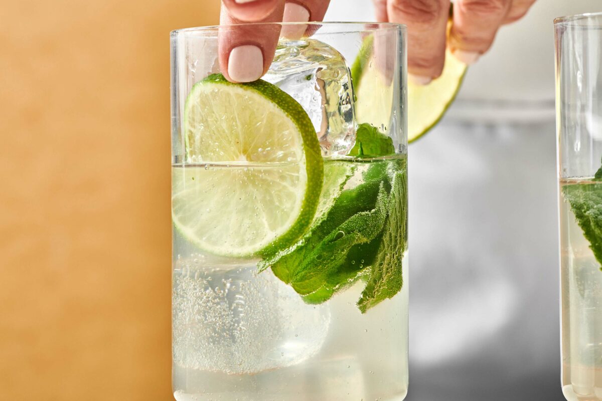 Woman putting a lime slice into a tall glass filled with a mojito.