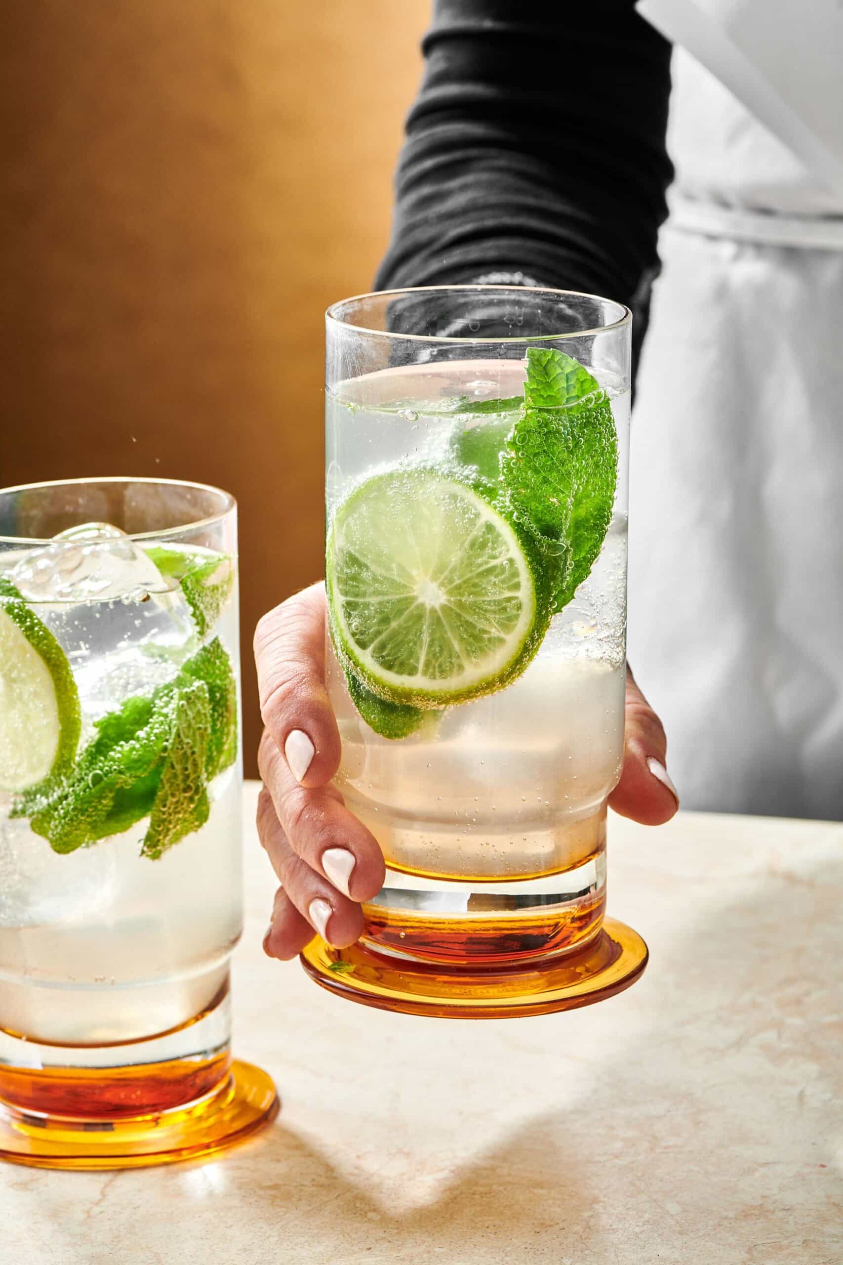 Woman grabbing a tall glass filled with a Mojito.