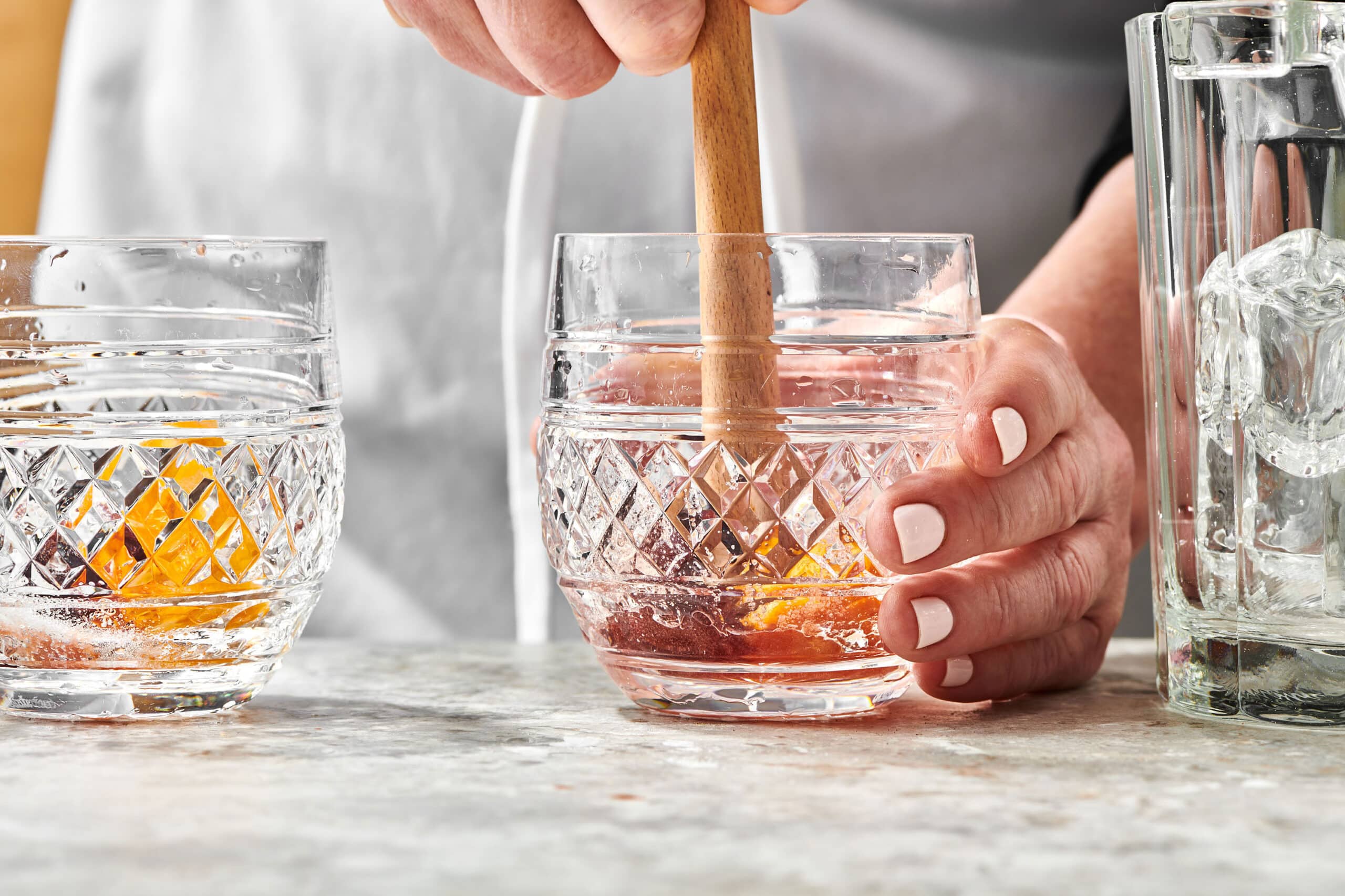 Woman muddling fruit in a rocks glass.
