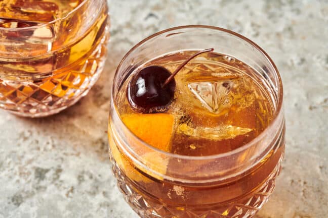 Cherry, orange, and ice floating in an Old Fashioned.