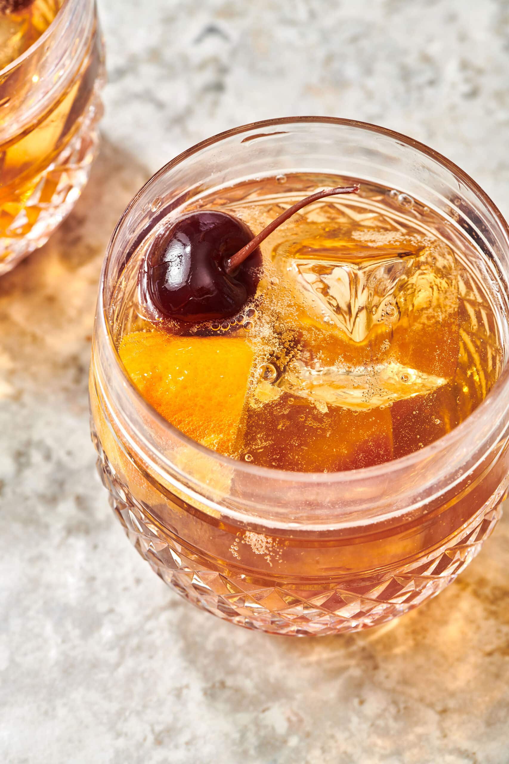 Old Fashioned cocktail with cherry and orange on table.