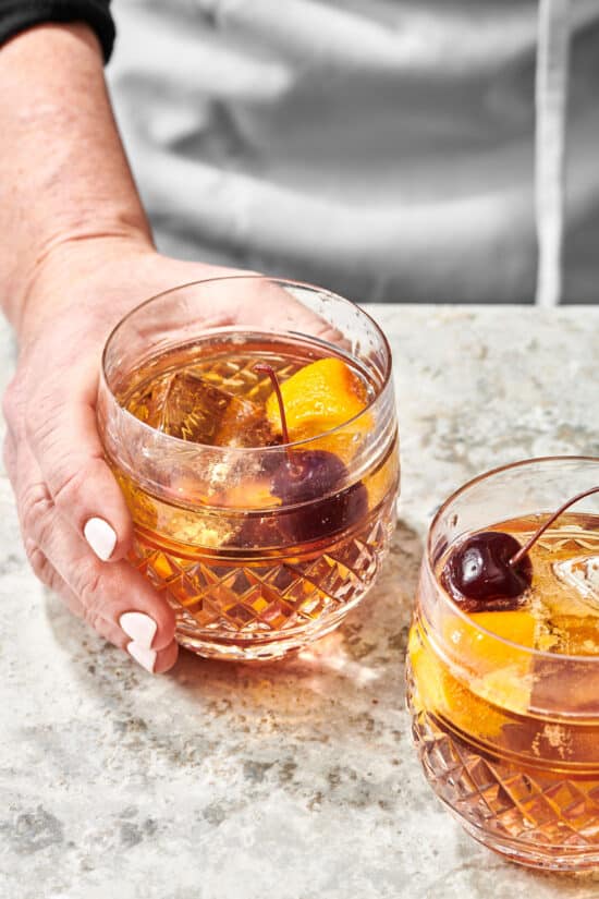 Woman grabbing an Old Fashioned in a rocks glass.