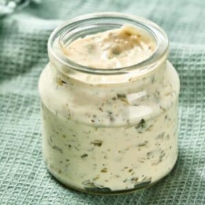 Glass jar filled with homemade tartar sauce on green towel.