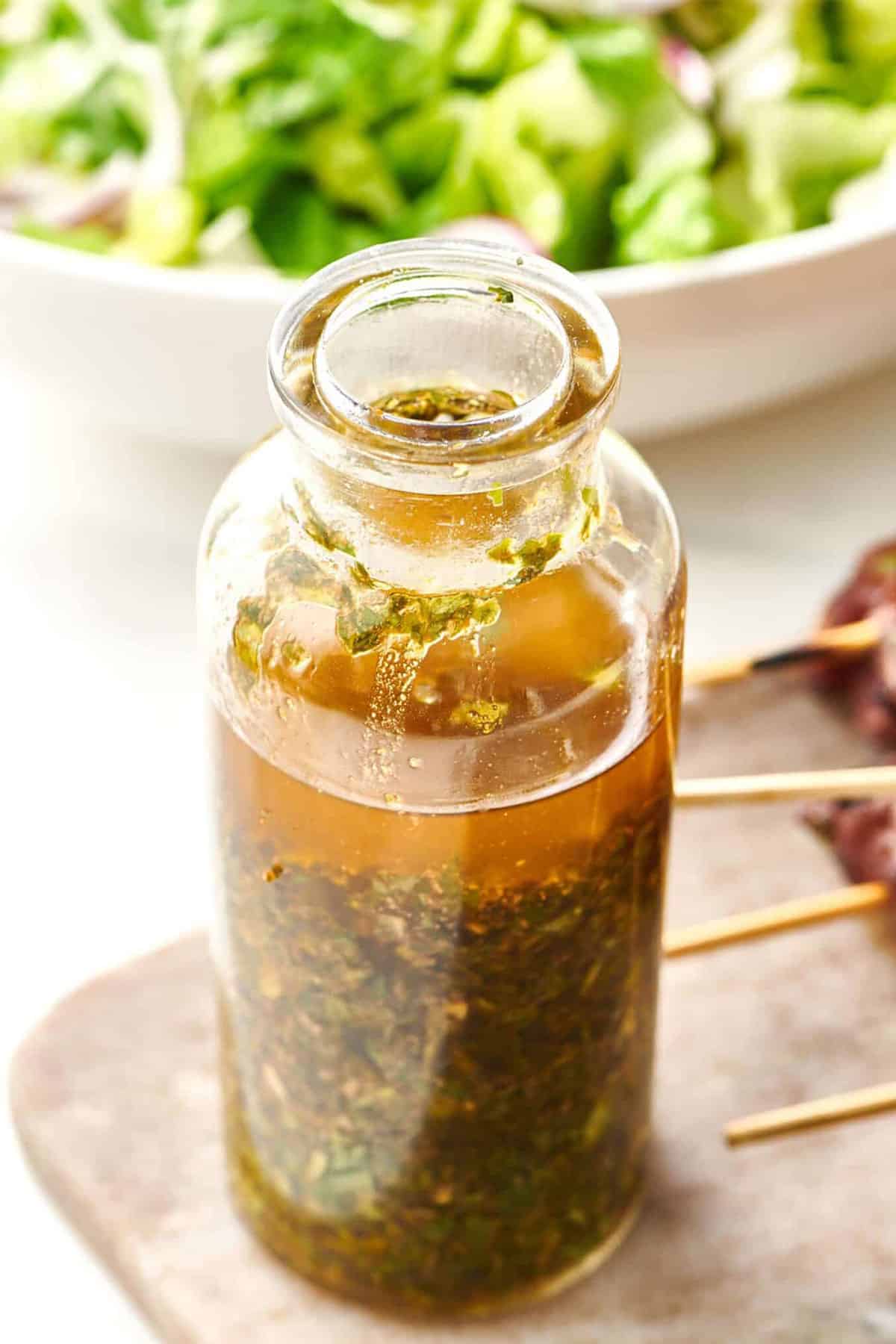 Homemade chermoula sauce in glass jar on table with salad and skewered kebabs.