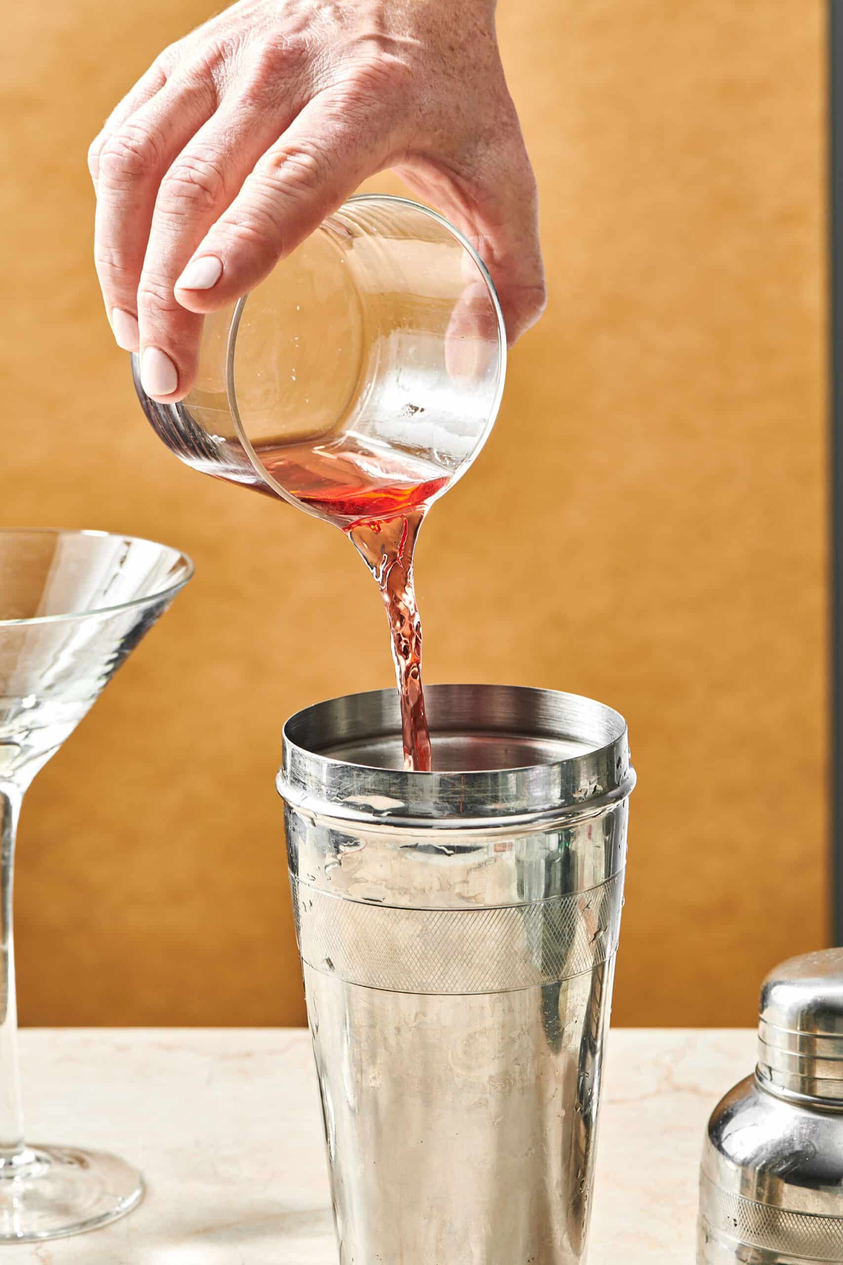Woman pouring cranberry juice into a metal cocktail shaker.