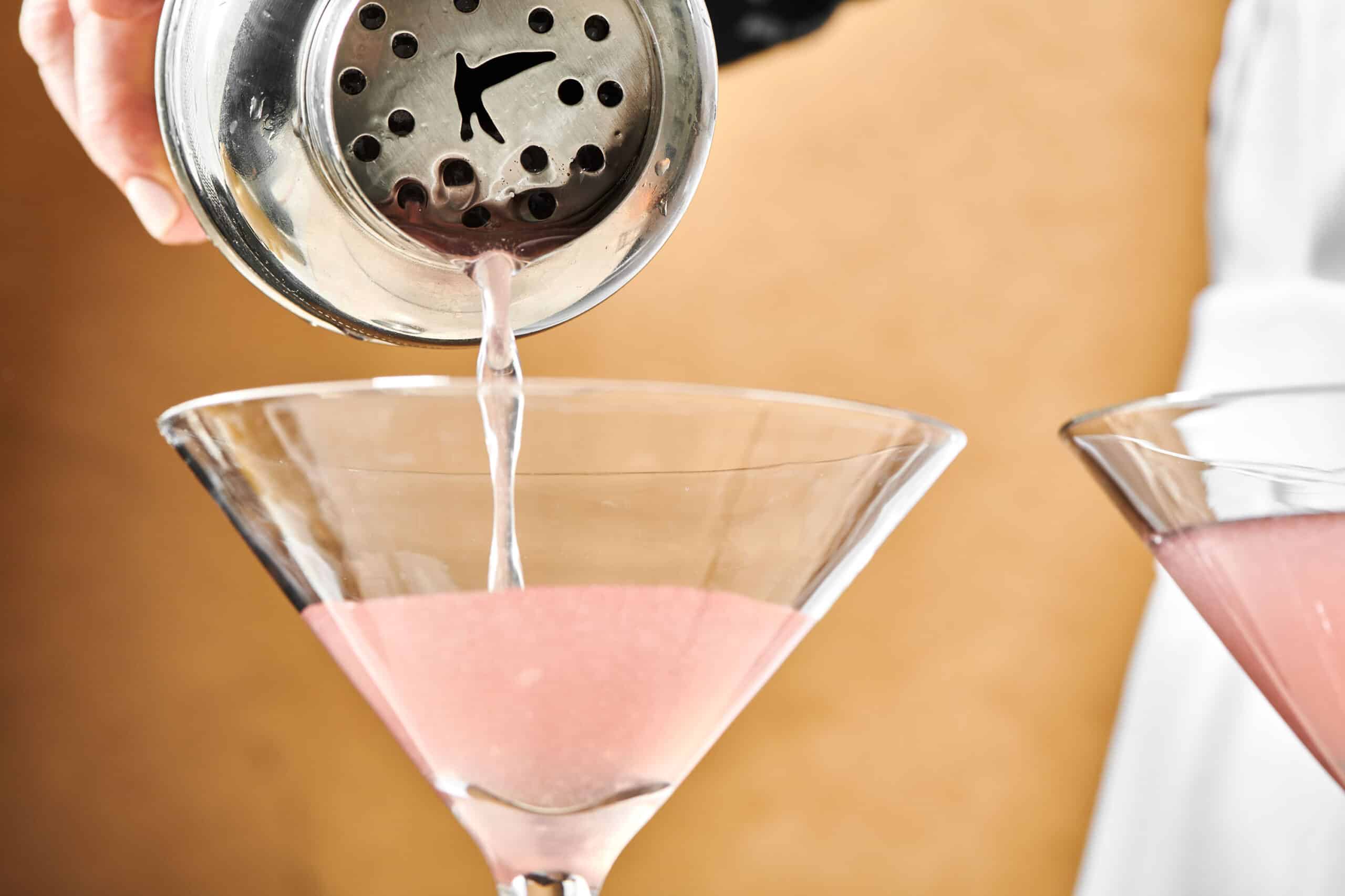 Cosmo pouring from a cocktail shaker into a long-stemmed glass.