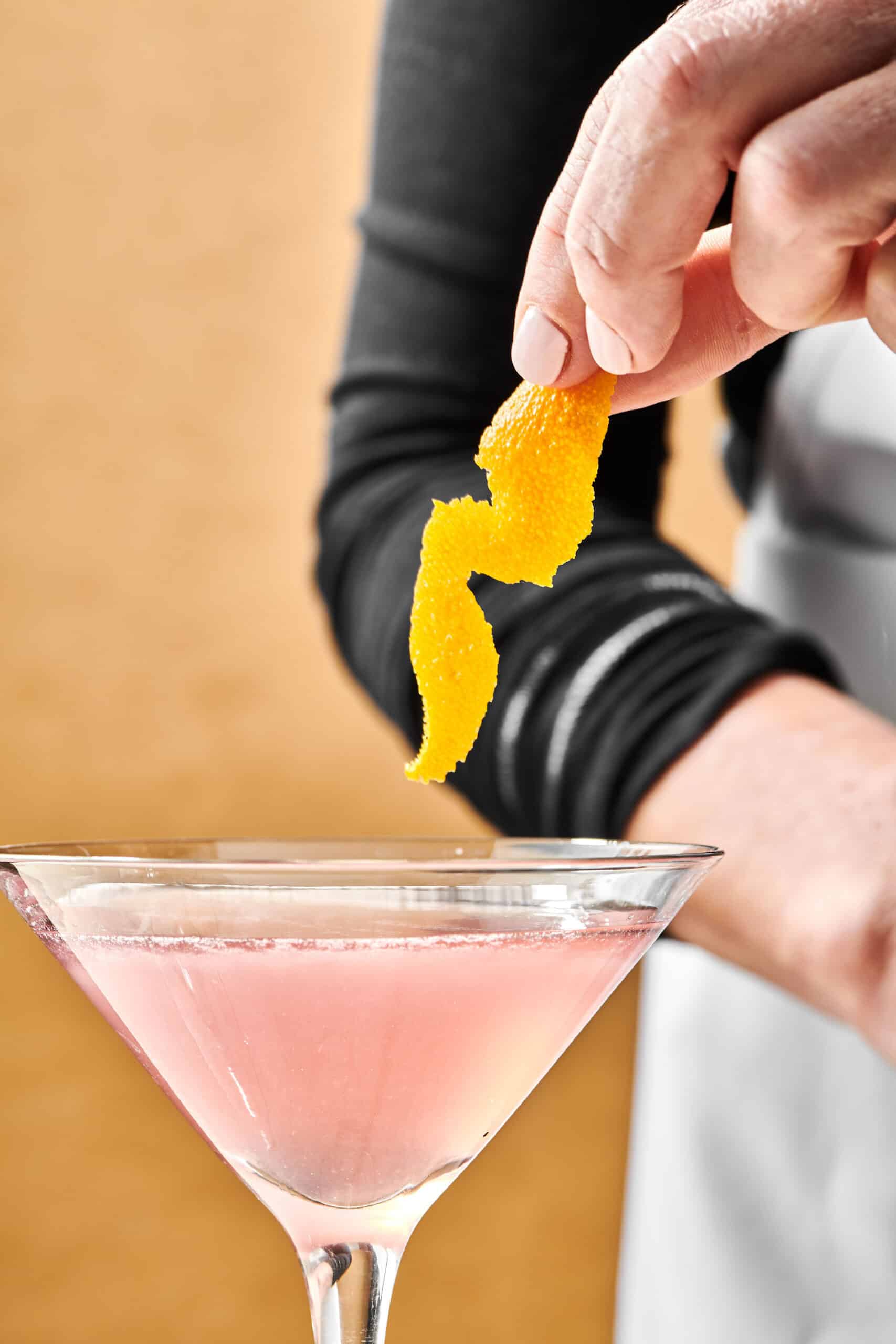 Woman putting a twisted orange peel into a Cosmo Cocktail.