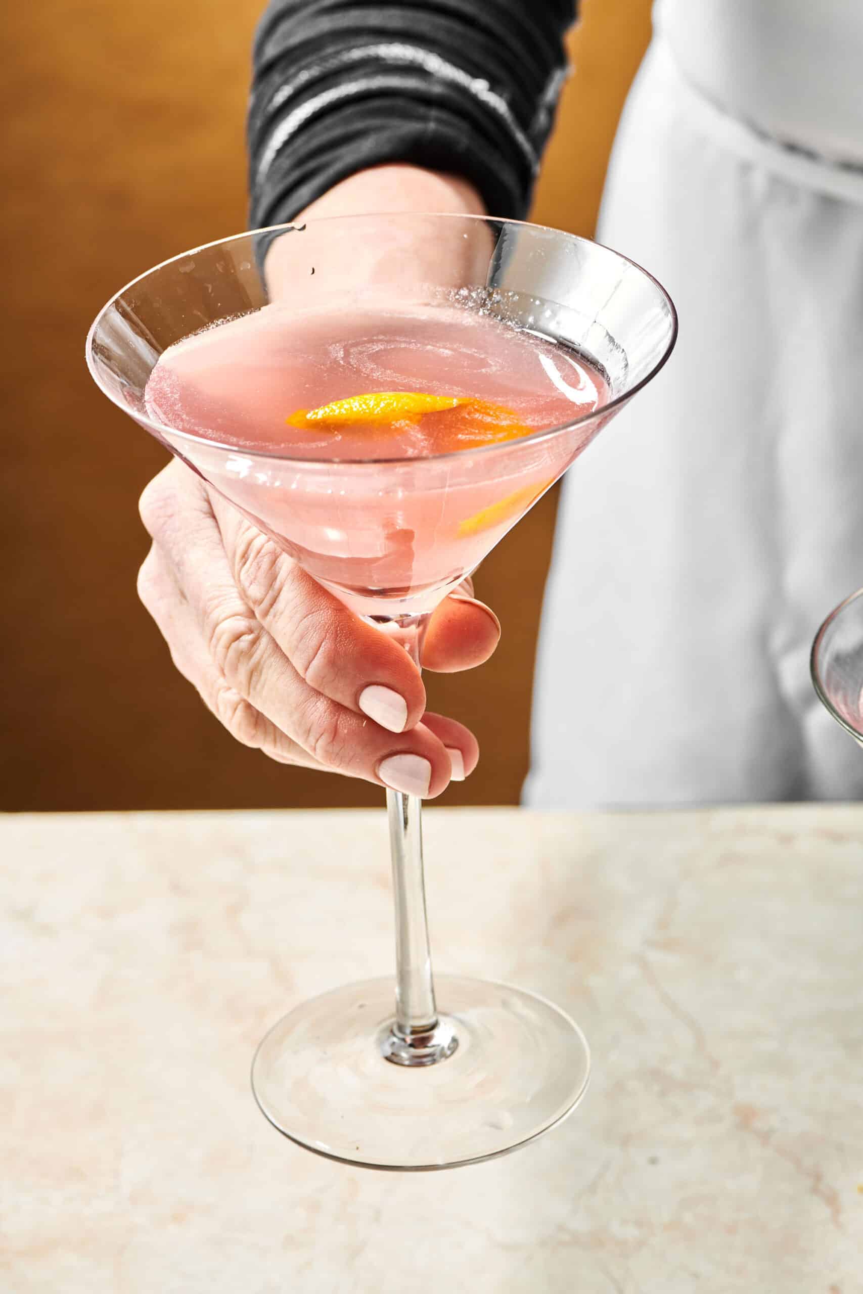 Woman holding a Cosmo Cocktail in a long-stemmed glass.