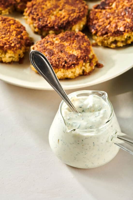 Jar of fresh Dill Sauce with spoon alongside crab cakes.
