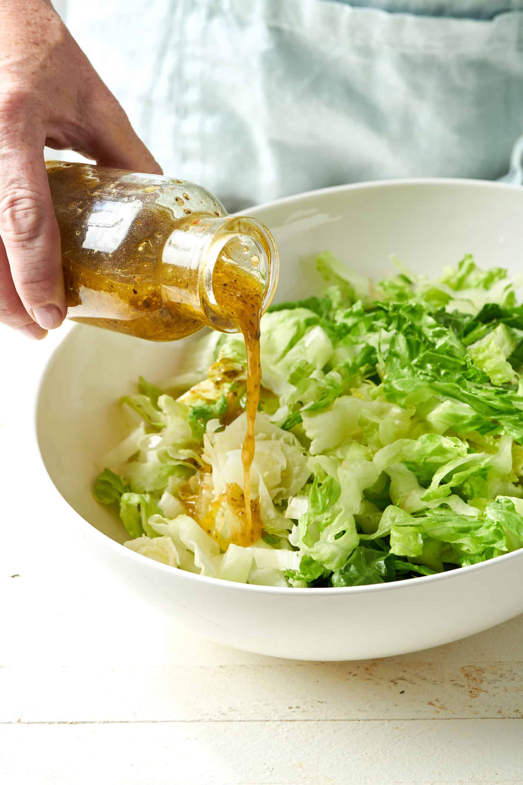 Woman pouring Italian dressing onto a bowl of salad.