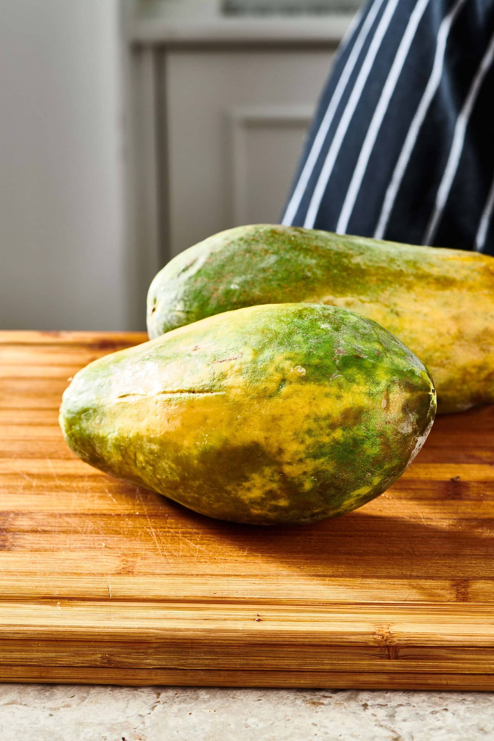 Two Papayas on a wooden cutting board.