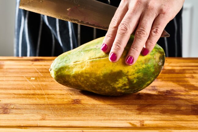 Woman holding a papaya and a large knife.