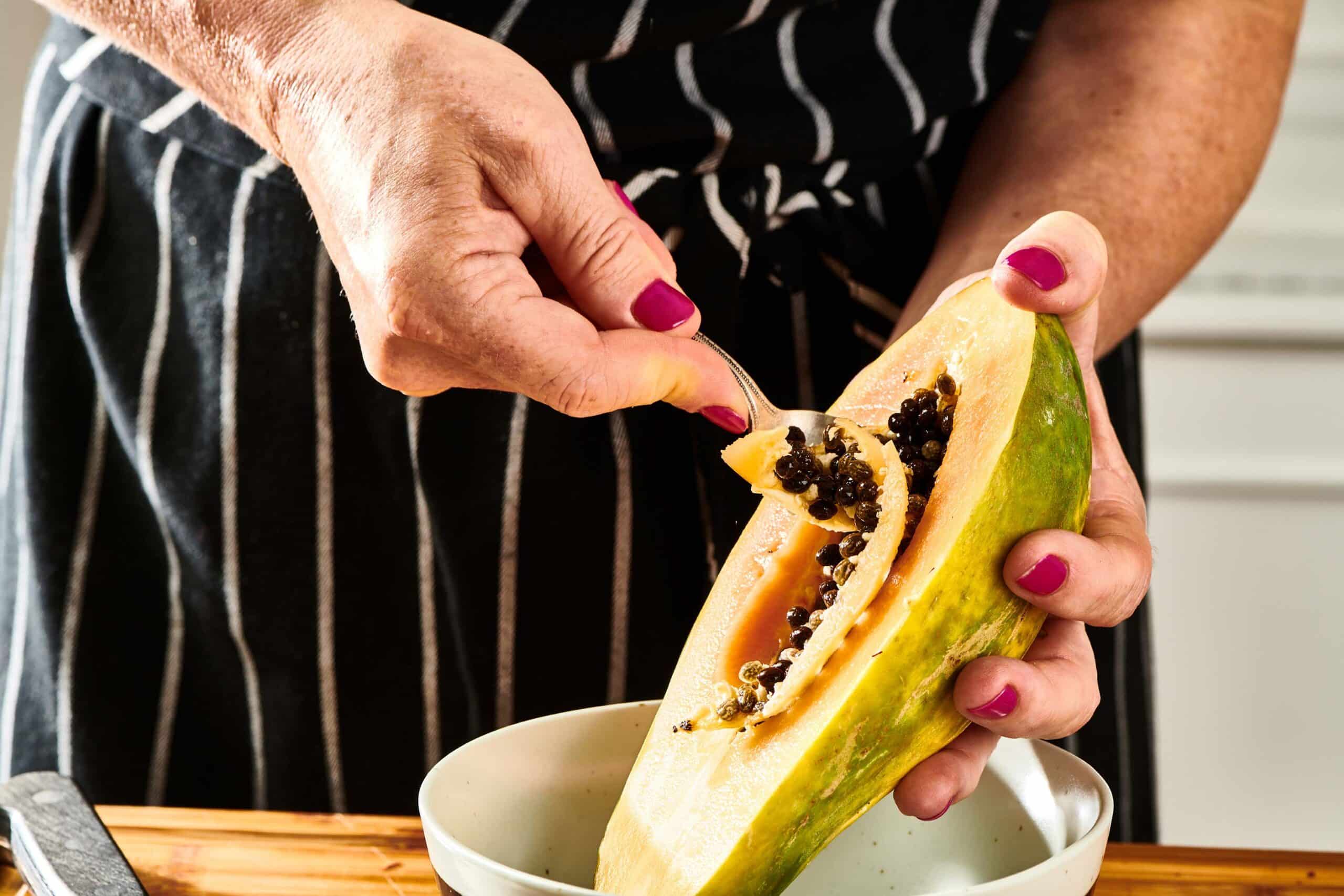 Woman scooping the seeds out of a halved papaya.