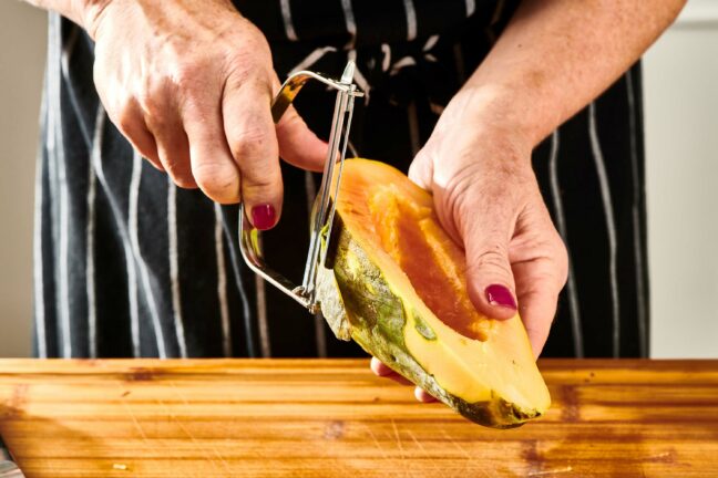 Woman using a peeler to peel a papaya half.
