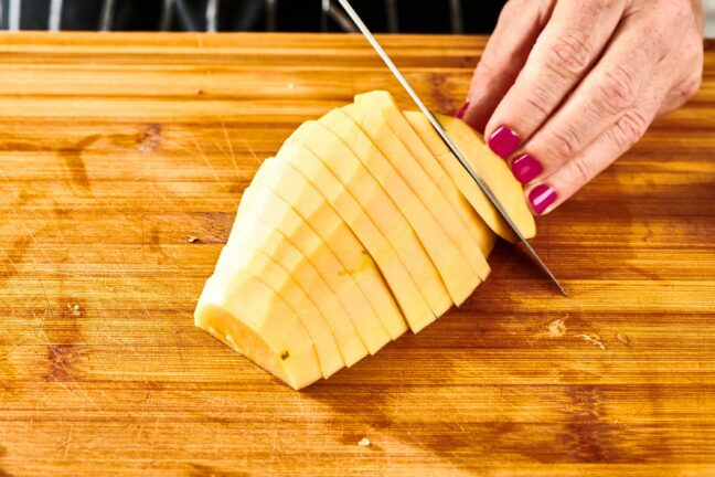 Woman slicing a halved, peeled papaya.
