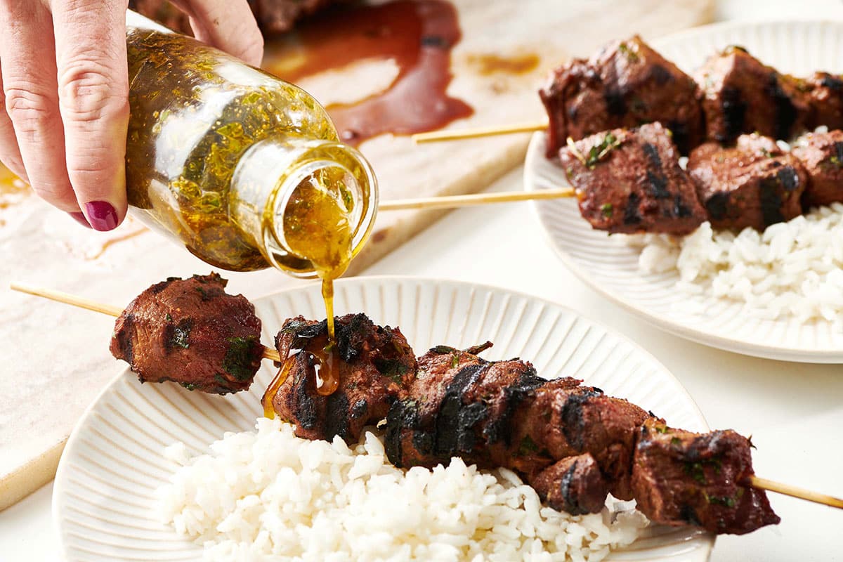 Pouring chermoula sauce over Moroccan Lamb Kebabs and rice.