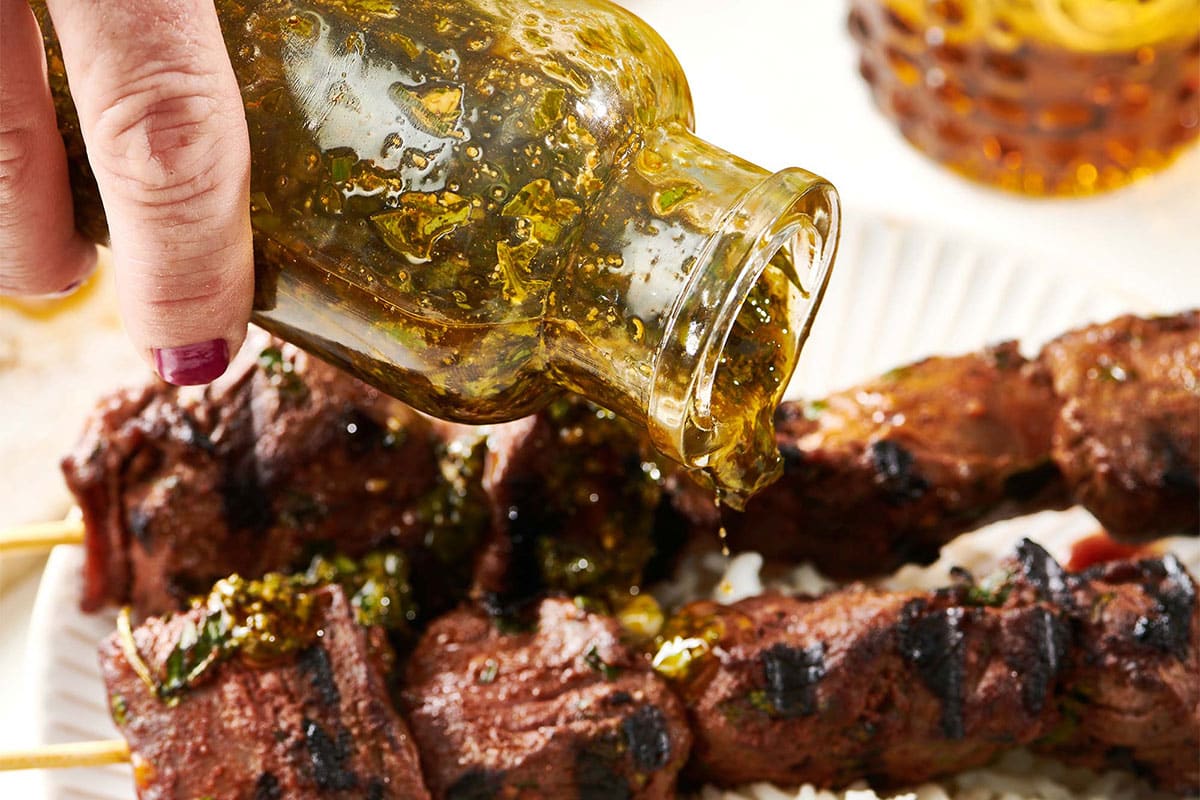 Pouring chermoula sauce over Moroccan-Inspired Lamb Kebabs on bed of rice.