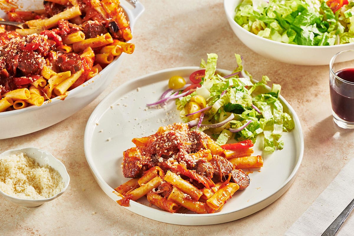 Italian sausage peppers and pasta on plate with salad.