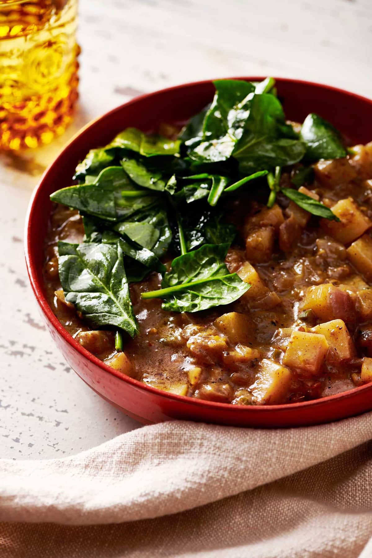 Potato Curry topped with spinach in a red bowl.