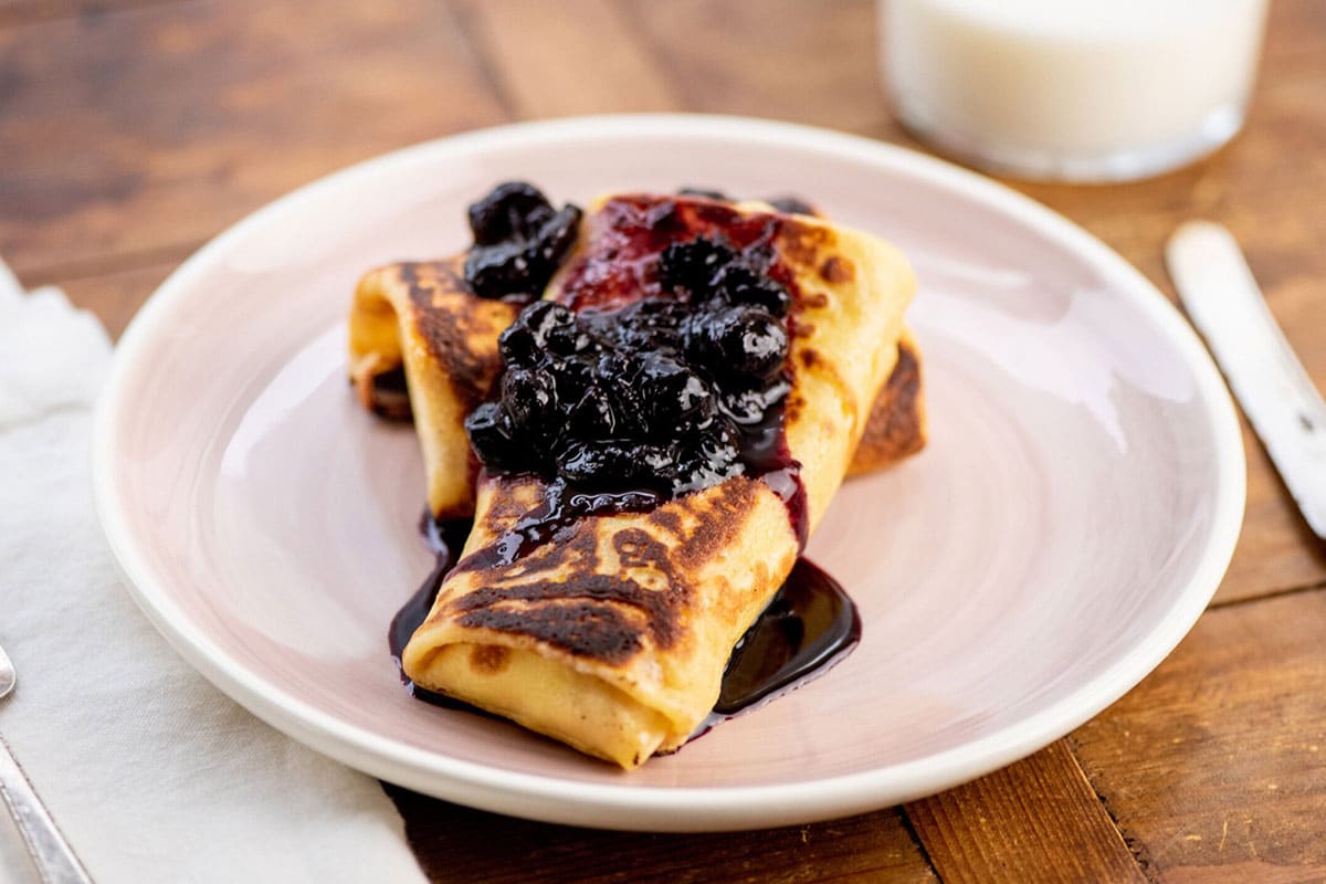 Breakfast blintz with blueberry topping on white plate.