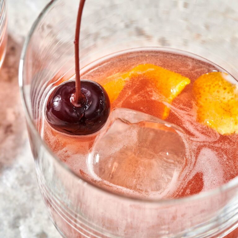 Boulevardier Cocktail with ice, orange peel, and a cherry.