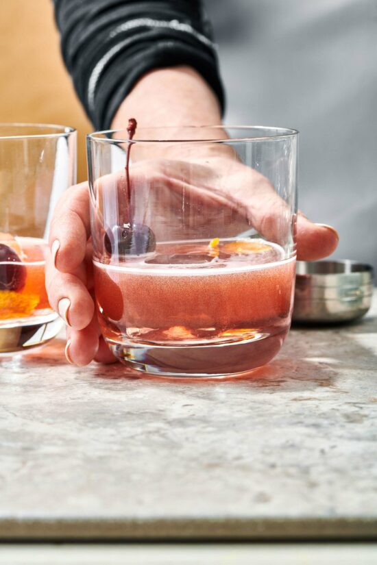 Woman grabbing a Boulevardier Cocktail in a small glass.