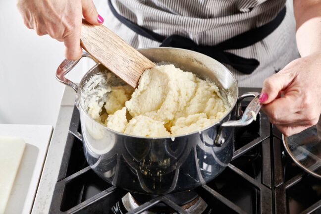 Woman using a wooden spatula to stir a pot of mashed potatoes.