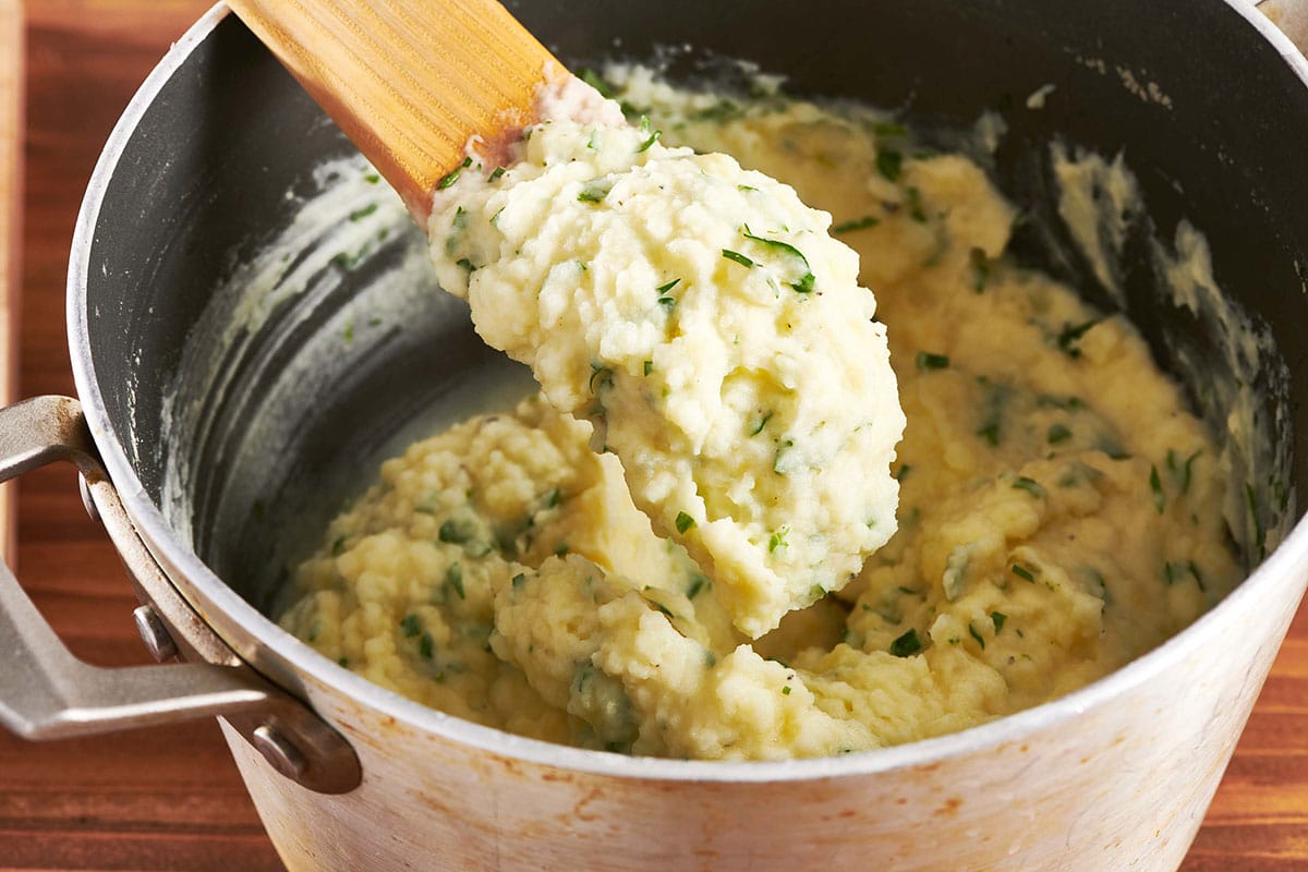 Spooning mashed potatoes with herbs from pot.