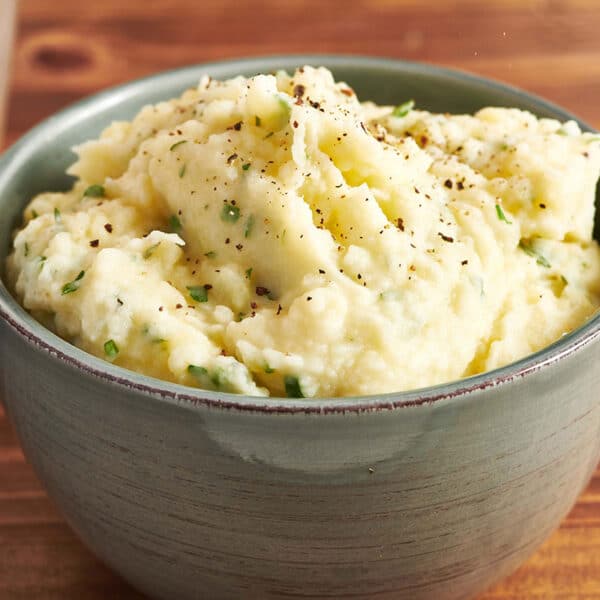 Mashed potatoes with herbs in grey bowl on table.