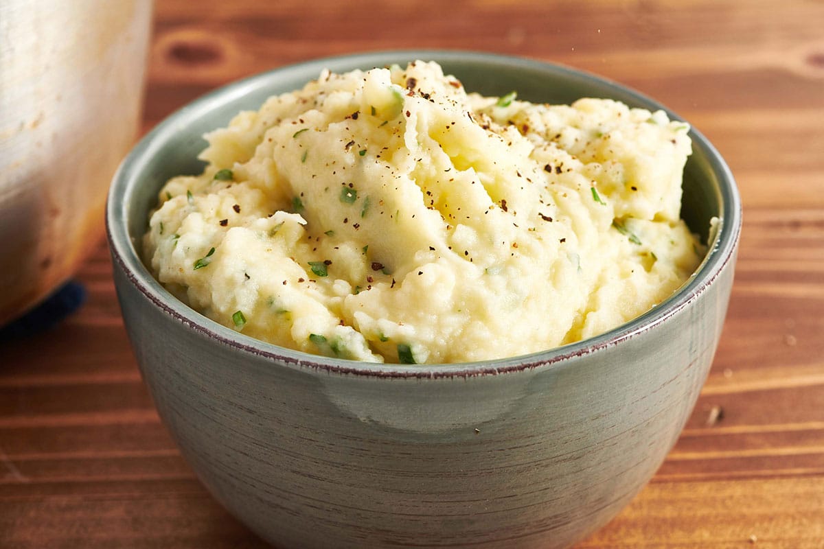 Mashed potatoes with herbs in grey bowl on table.