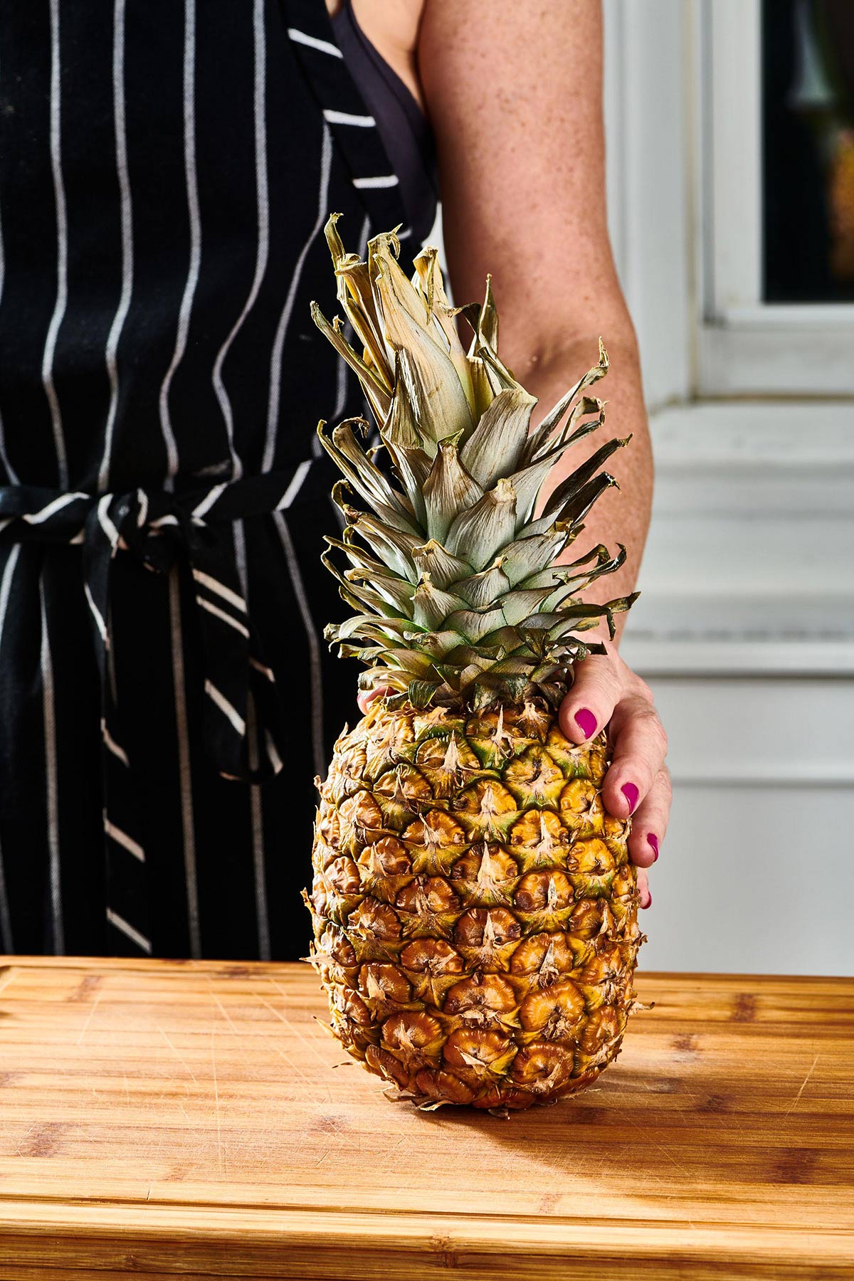 Woman holding fresh pineapple on cutting board.